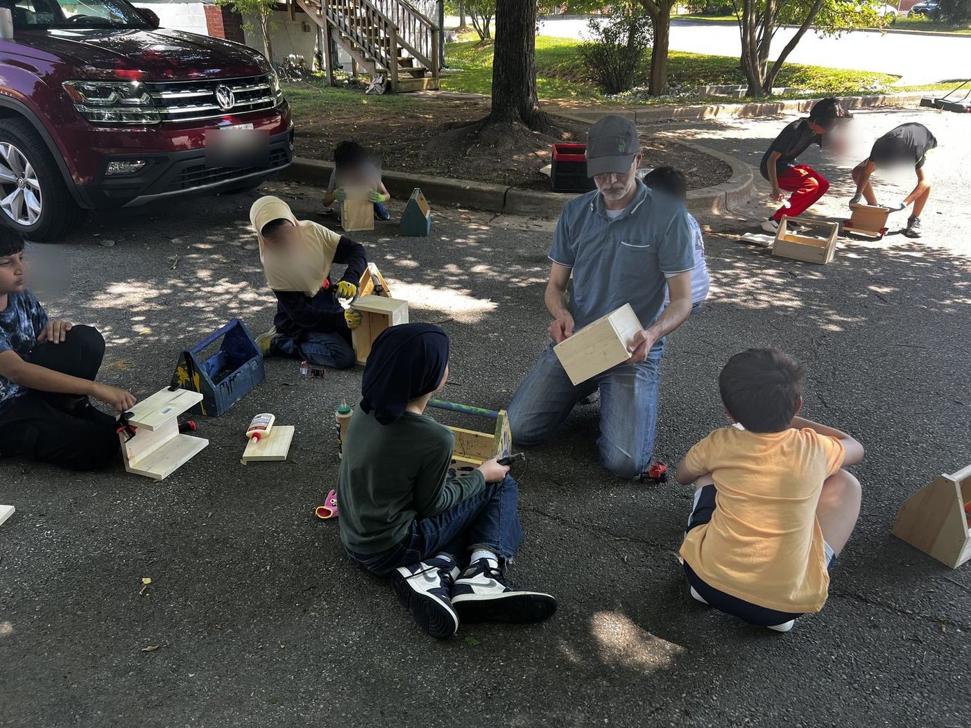 Students building wooden toolboxes outdoors with their instructor at woodworking club